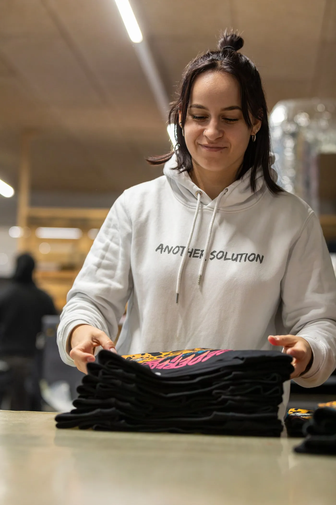En medarbejder hos AS Merch lægger et færdigt oplag trykte trøjer frem på bordet.