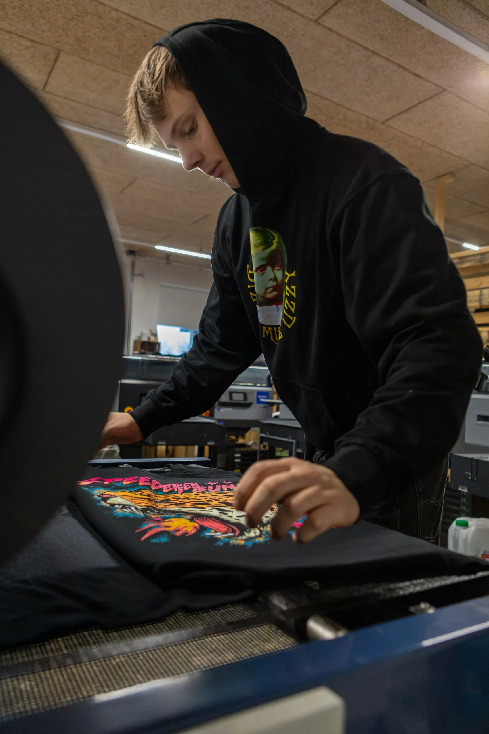 En medarbejder lægger en trøje med farverigt artist-tryk i varmepressen.