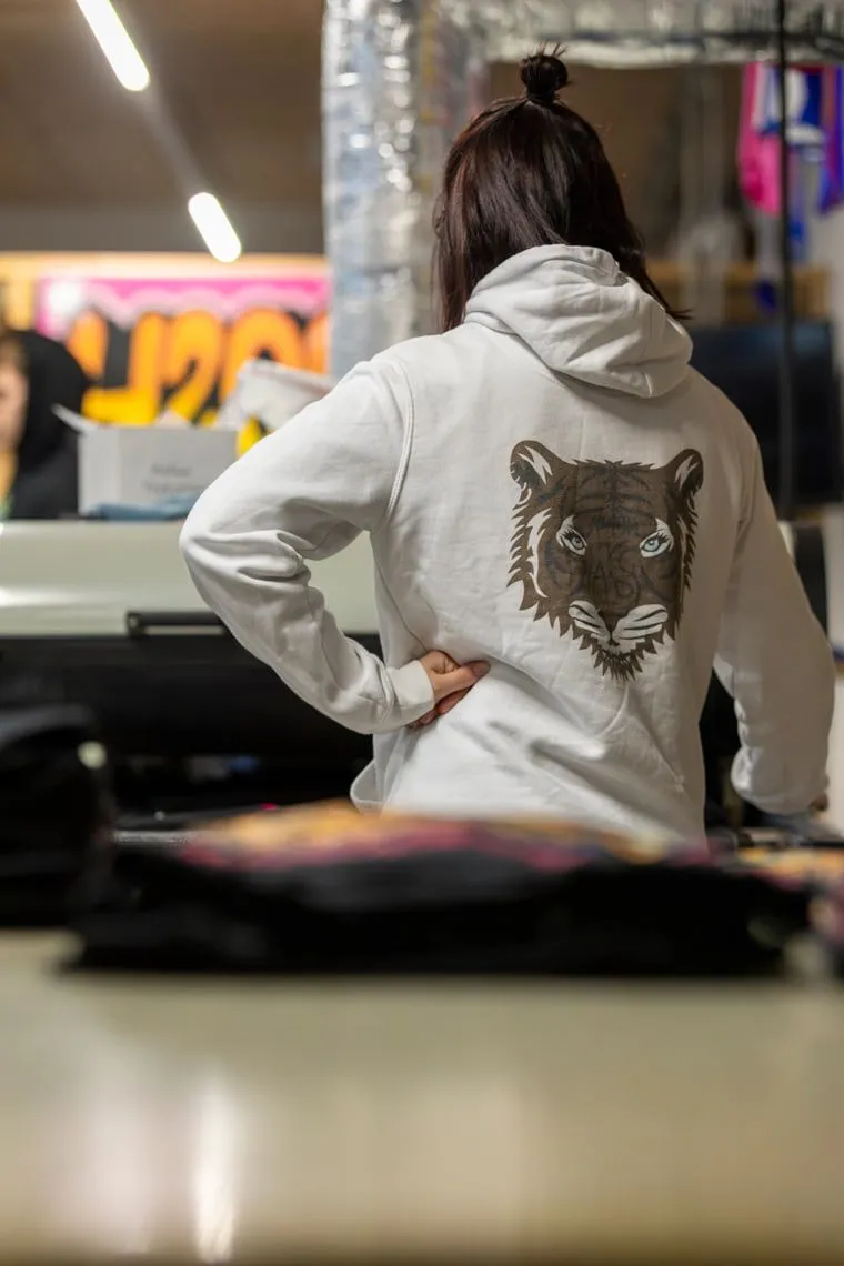 Ryggen af en lys hættetrøje med et stort trykt tigermotiv.